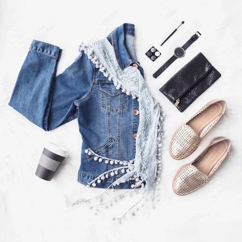 Flat lay of a leather jacket, floral dress, boots, and accessories on a bed
