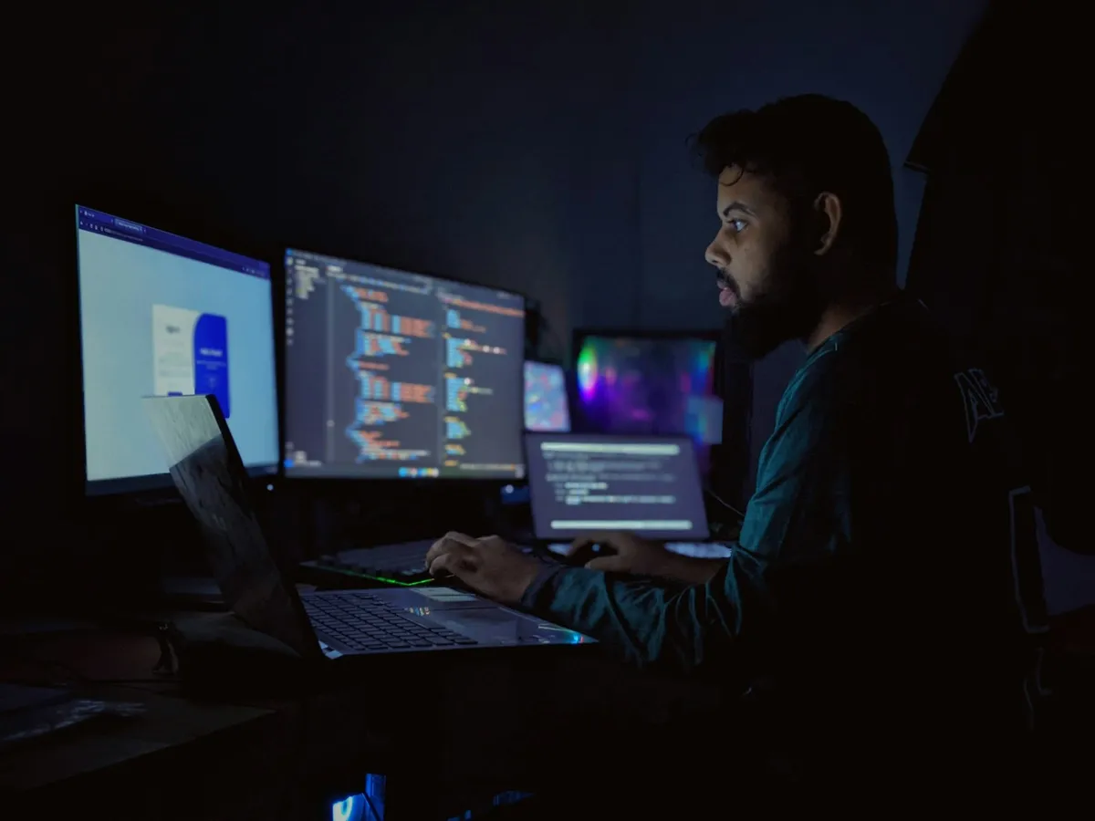 Engineer working across three monitors in a dark room