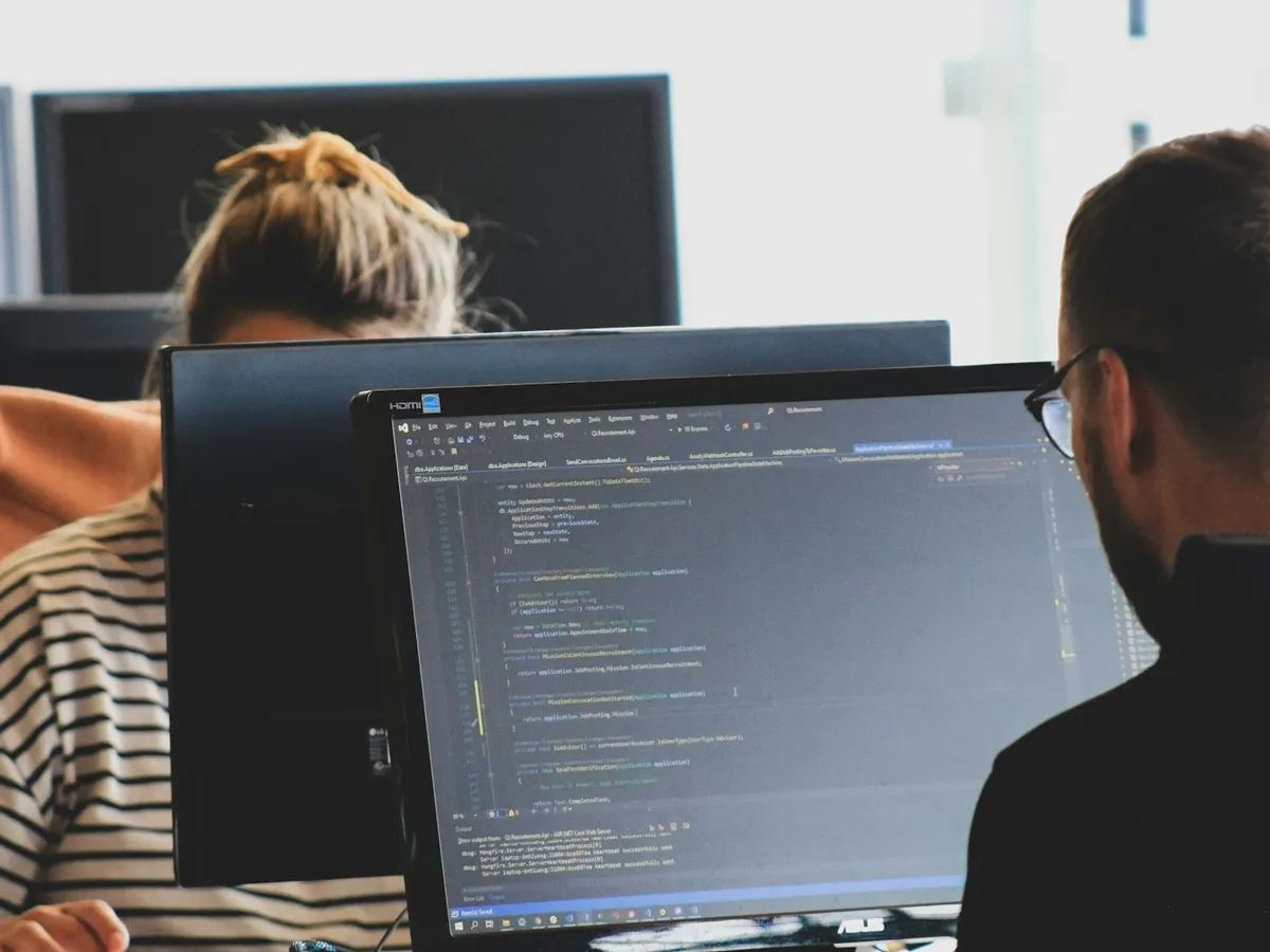 Two developers writing code side by side at their monitors
